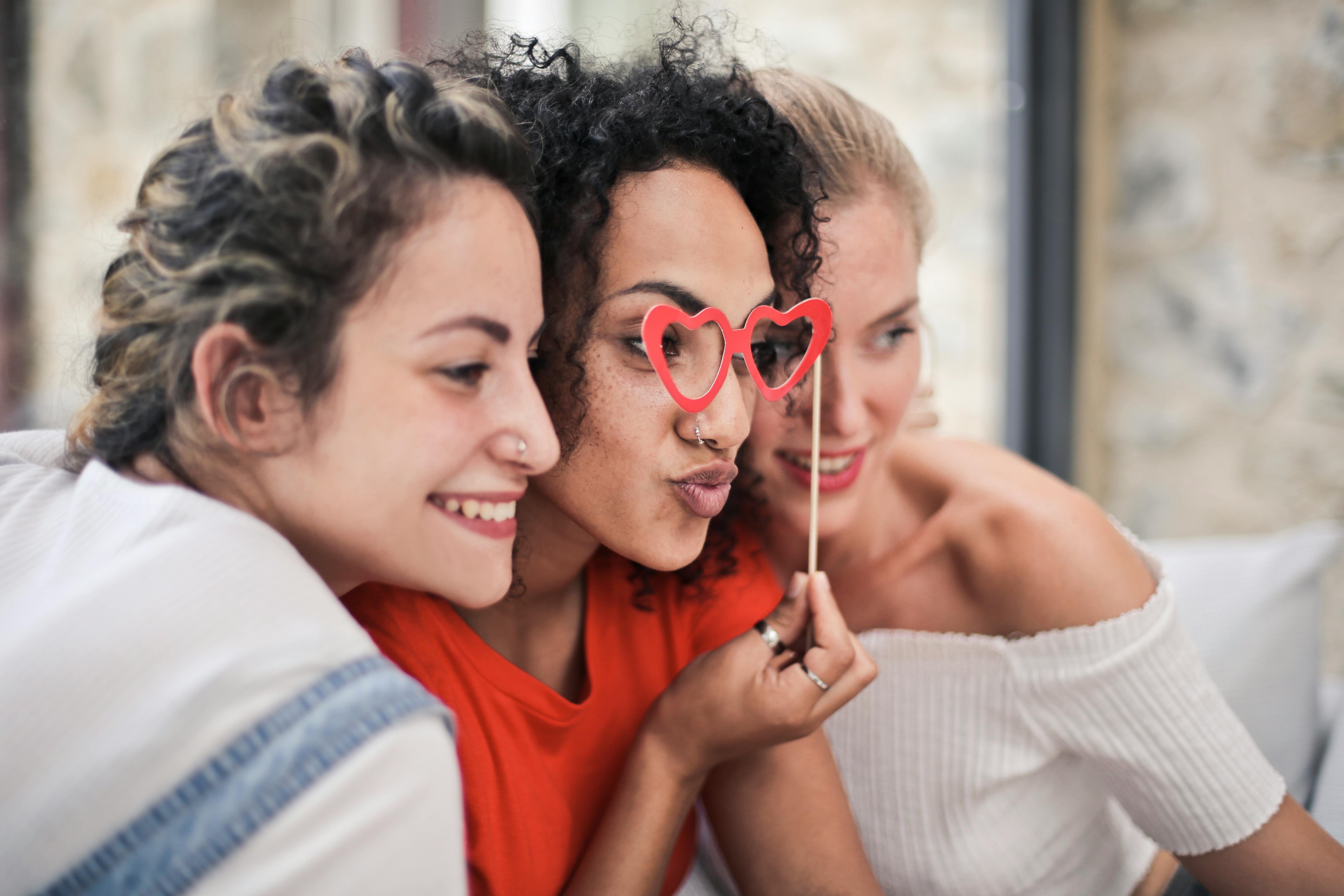 Three women enjoying a playful moment with heart-shaped glasses, symbolizing friendship and fun.